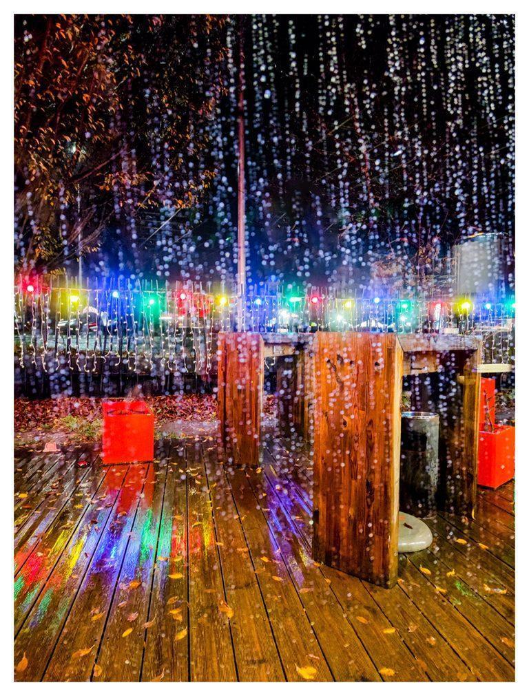 Ambiance de Noël sous la pluie les lampadaires renvoient leurs couleurs sur le sol trempé.