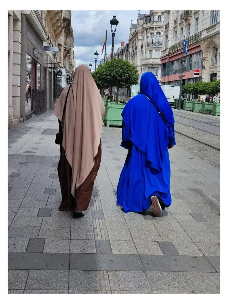 2 femmes marchent sur la voie publique vêtues de tenues de couleurs vives contrastent avec la lumière de la ville